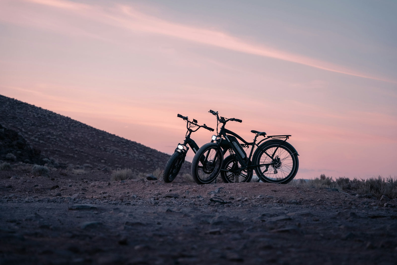 Zwei E-Bikes mit dicken Reifen stehen bei Sonnenuntergang in einer trockenen Landschaft
