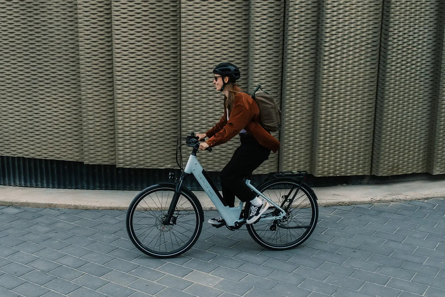 Mann mit Helm fährt modernes E-Bike vor Altbau mit Graffiti an sonnigem Tag